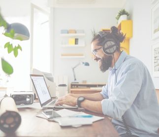 World Music Day Ein Mann mit Kopfhörern arbeitet an einem Laptop in einem hellen Raum.
