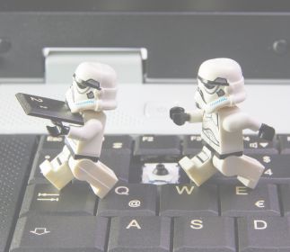 World Star Wars Day Zwei Stormtrooper-Figuren, die auf einer Laptop-Tastatur stehen. Einer hält ein Tablet in der Hand.