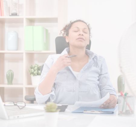 Sommer im Homeoffice Eine Frau sitzt am Schreibtisch, hält Dokumente und scheint entspannt oder erleichtert zu sein. im Hintergrund sind Pflanzen und Büroartikel zu sehen.