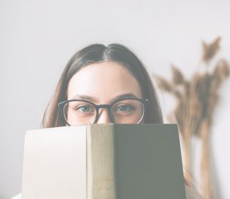 World Book Day Eine Person mit Brille hält ein Buch vor ihrem Gesicht.