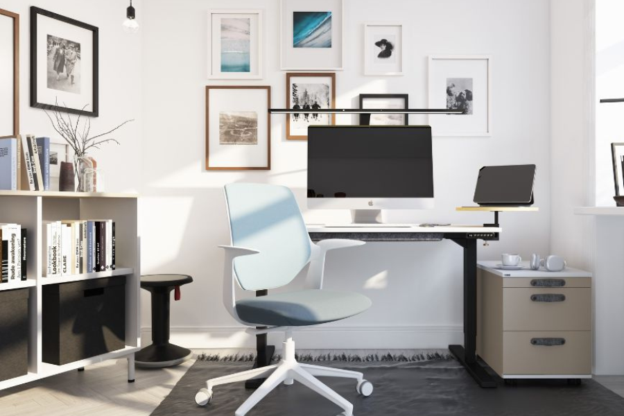 Ein minimalistisches Büro mit einem Schreibtisch, einem Computer, einem Laptop, einem ergonomischen Stuhl und gerahmten Bildern an der Wand.