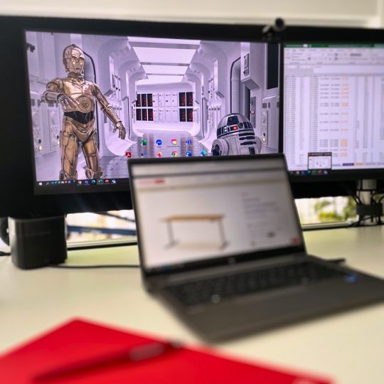 Der Bildschirm zeigt C-3PO und R2-D2 in einem Raumschiff. Im Vordergrund steht ein Laptop mit einer Möbel-Webseite und einem roten Notizbuch.