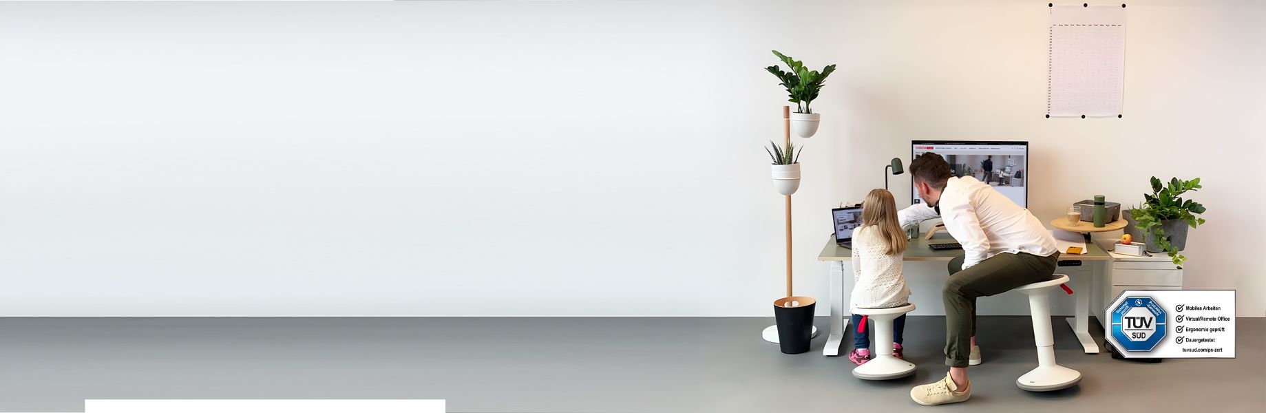 Vater arbeitet mit Tochter gemeinsam am höhenverstellbaren Schreibtisch, TÜV-Zertifikat sichtbar