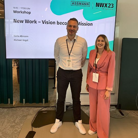 Zwei Personen beim ASSMANN Workshop auf der NWX23 Konferenz vor Präsentationsbildschirm.