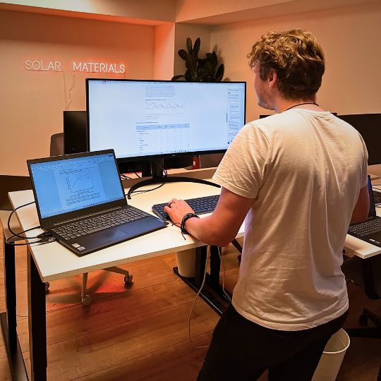 Mann arbeitet im Stehen an einem höhenverstellbaren Schreibtisch mit zwei Monitoren und Laptop.