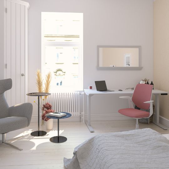 Ein modernes Zimmer mit einem Schreibtisch, einem Laptop, einem pinken Stuhl, einem gemütlichen Lesesessel und kleinen Tischen. Ein Fenster lässt viel Licht herein.