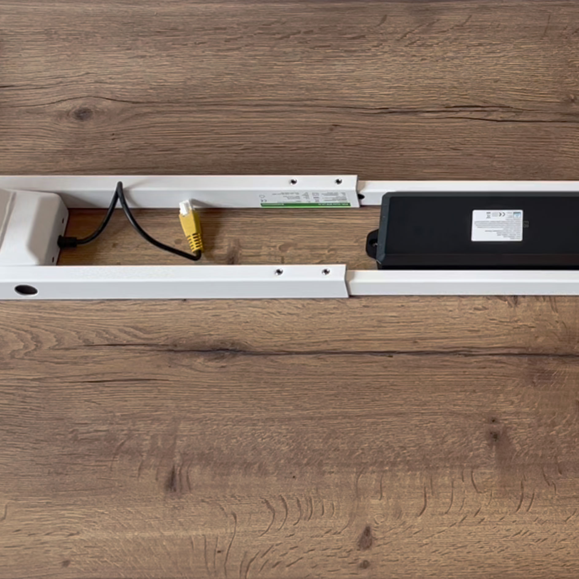 Eine weiße Schiene mit elektrischen Komponenten und Kabeln auf einem Holzfußboden.