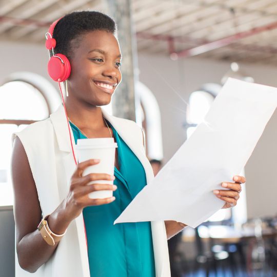 Frau mit roten Kopfhörern hält einen Kaffeebecher und ein Dokument im modernen Büro.