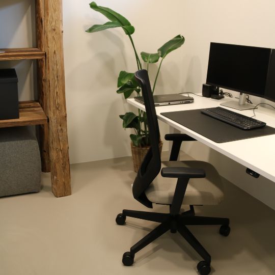 Modernes Home-Office mit weißem Schreibtisch, ergonomischem Bürostuhl, Monitor und Pflanzen auf hellem Bodenbelag