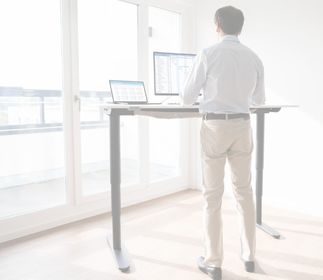 So sitzt du richtig: Die perfekte Sitzposition und Schreibtischeinstellung Eine Person steht an einem Stehtisch und arbeitet an einem Computer.