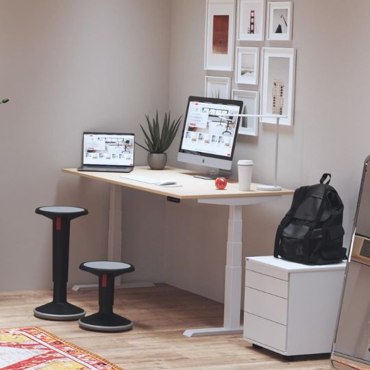 Ein modern eingerichteter Arbeitsplatz mit zwei Bildschirmen, einer Pflanze, einer Tasse, einem Rucksack und einem weißen Schreibtisch.