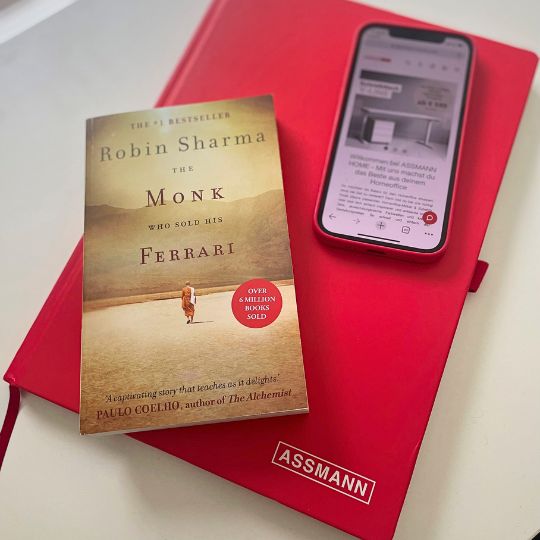 Rotes Notizbuch mit Smartphone und Buch 'The Monk Who Sold His Ferrari' von Robin Sharma.