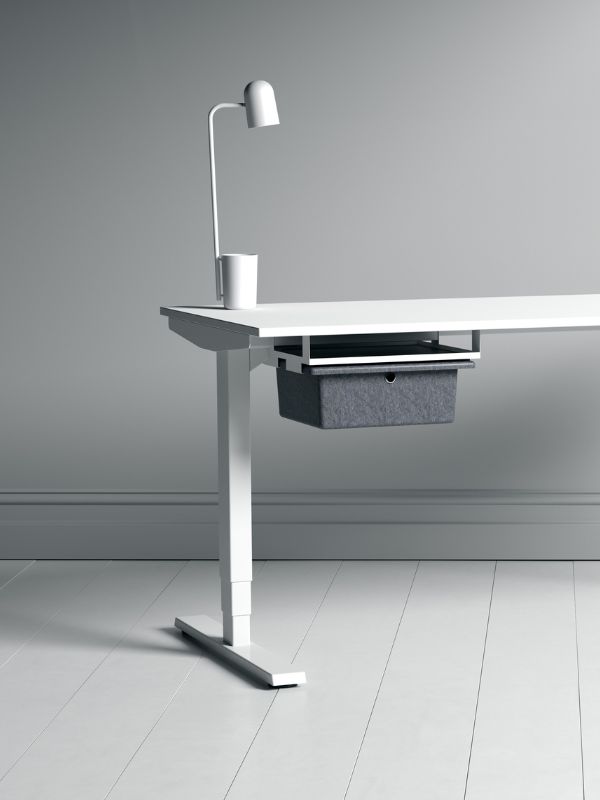 Ein schlichter weißer Schreibtisch mit einer grauen Aufbewahrungsbox unter der Tischplatte, einer Lampe und einem Becher.