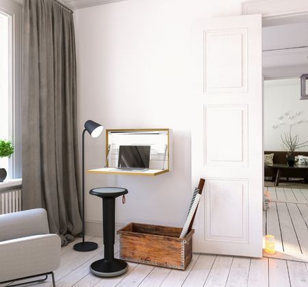 Kompakter Arbeitsplatz mit Wandklapptisch, Hocker, Stehlampe und Holzkiste im Wohnzimmer.
