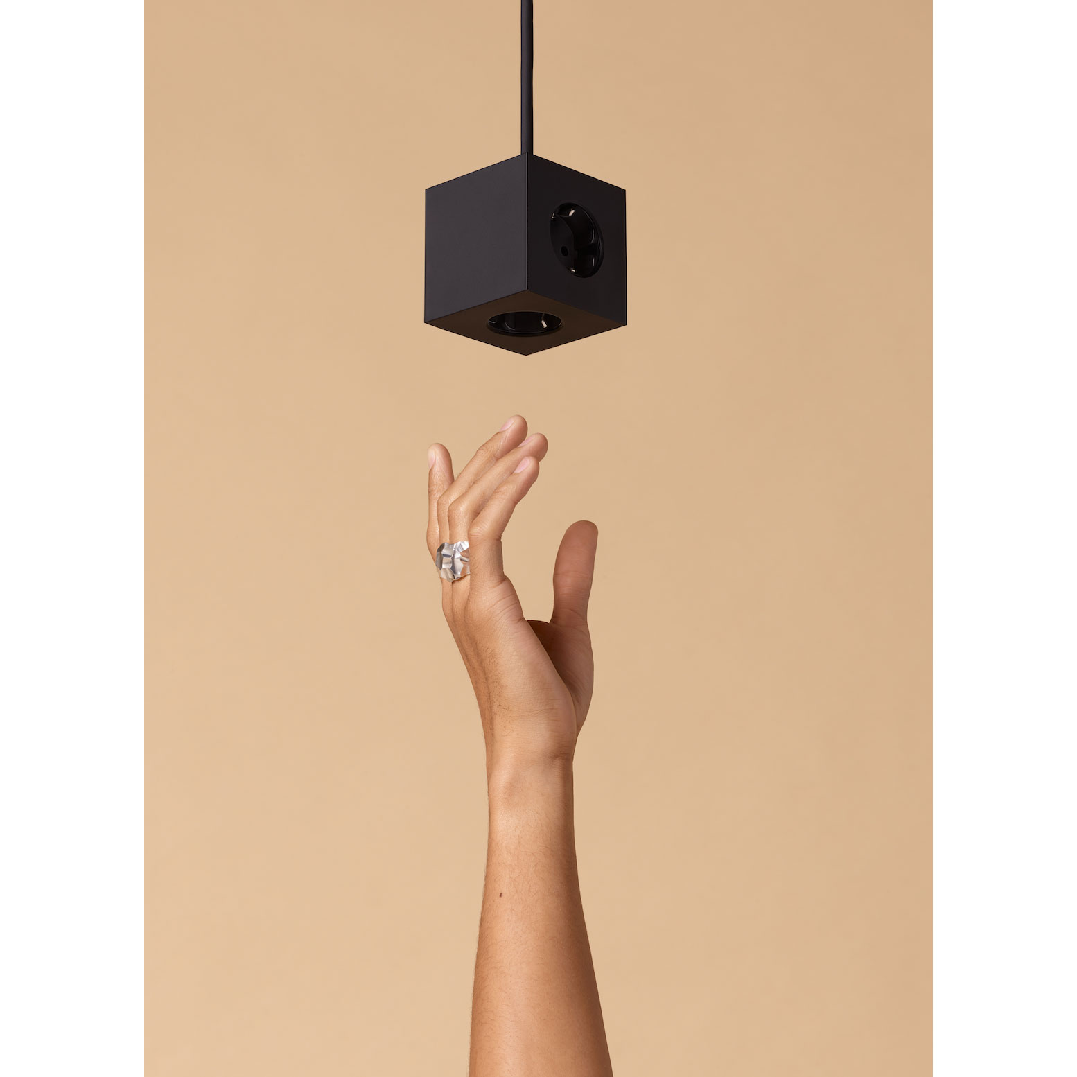 Schwarze AVOLT Design-Mehrfachsteckdose Cube – stilvoll von der Decke hängend mit Hand im Vordergrund, modernes Wohnaccessoire