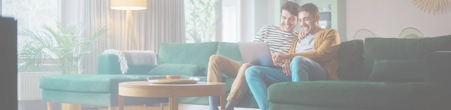 Zwei Männer sitzen auf einem grünen Sofa und schauen gemeinsam auf einen Laptop.