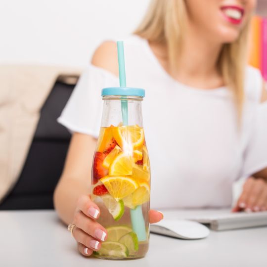 Ein Glas mit fruchtigem Getränk (Zitrusfrüchte und Erdbeeren) und einem Strohhalm, gehalten von einer Person.