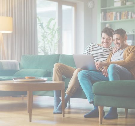 Zwei Männer sitzen gemeinsam auf dem Sofa und schauen auf einen Laptop.