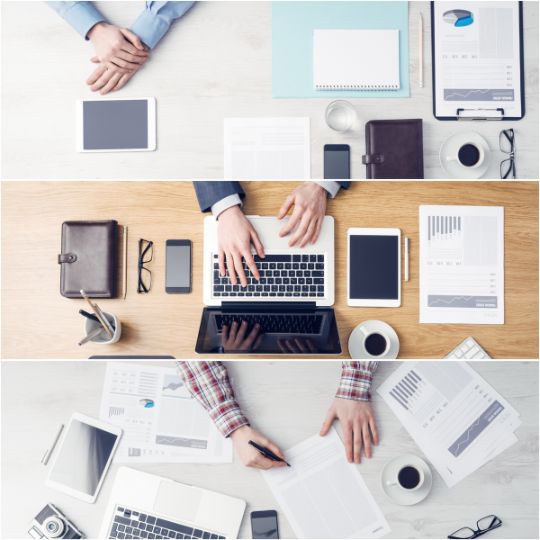 Bürotisch mit Händen, Laptops, Tablets, Notizbüchern, Unterlagen und Tassen Kaffee.