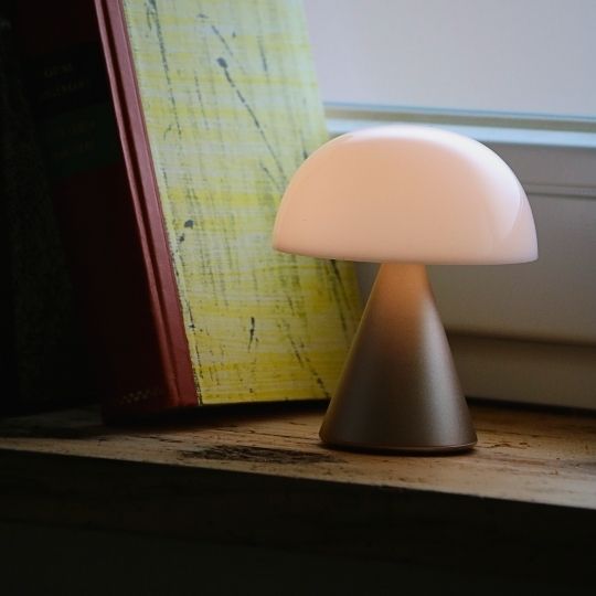 Kleine LED-Tischlampe mit rundem Schirm auf Fensterbrett neben Büchern.