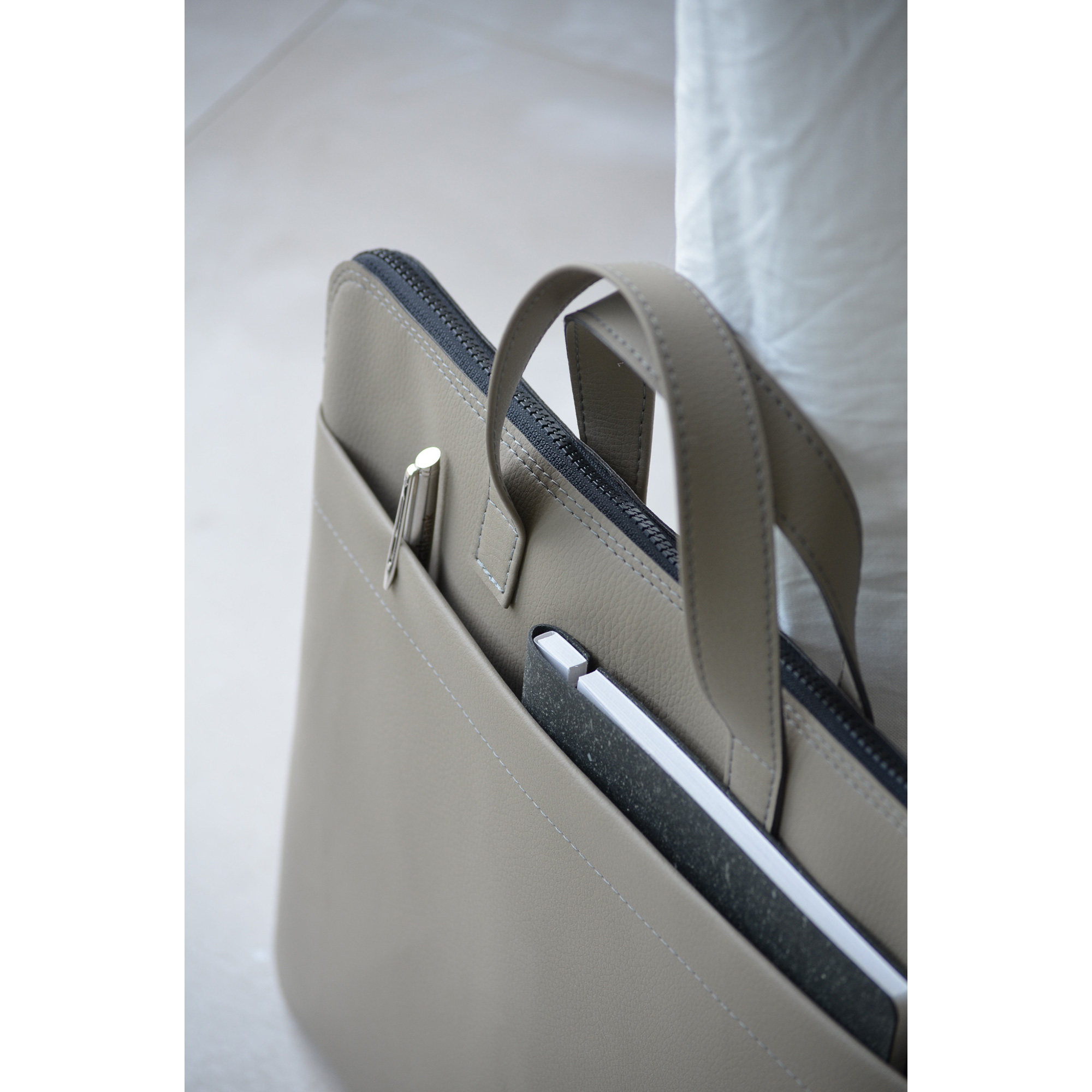 Hellgraue Laptoptasche mit Notizbuch und Kugelschreiber im Außenfach – praktische Organisation für unterwegs