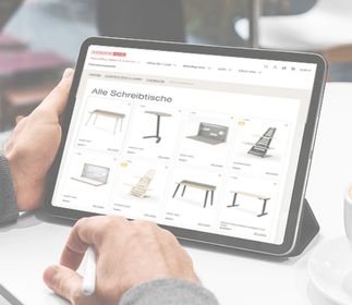 Eine Person hält ein Tablet in der Hand, auf dem der ASSMANN Home Online-Shop mit ergonomischen Schreibtischen für das Homeoffice angezeigt wird. Eine Person, die auf einem Tablet eine Webseite mit verschiedenen Schreibtischen durchblättert.
